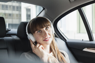 Porträt einer lächelnden Geschäftsfrau mit Kopfhörern, die in ihrem Auto Musik hört - FMKYF000602