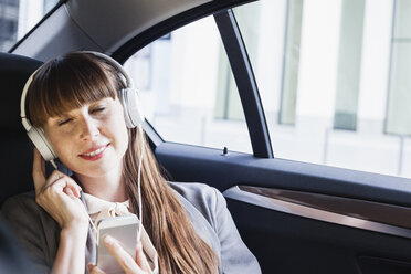 Portrait of smiling businesswoman with headphones hearing music in her car - FMKYF000603