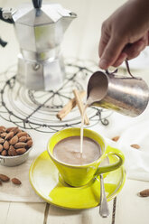 Frauenhand gießt Mandelmilch in eine Tasse Kaffee - SBDF001259