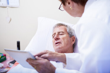 Doctor showing digital tablet to senior man in hospital bed - ZEF000962