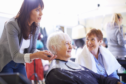 Female hairdresser cutting hair of senior woman stock photo