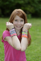 Portrait of happy girl showing self-made looms at her wrists - LBF000955