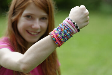 Smiling girl showing self-made looms at her wrist - LBF000957