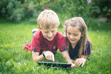 Bruder und Schwester liegen auf einer Wiese und benutzen ein digitales Tablet - SARF000866