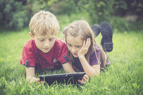 Bruder und Schwester liegen auf einer Wiese und benutzen ein digitales Tablet - SARF000867
