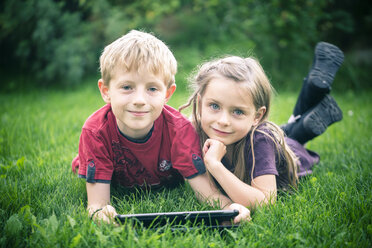 Porträt von Bruder und Schwester auf einer Wiese liegend mit digitalem Tablet - SARF000868