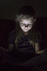 Porträt eines kleinen Mädchens, das in der Dunkelheit sitzt und ein digitales Tablet benutzt - SARF000869