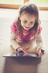 Porträt eines kleinen Mädchens, das auf dem Boden sitzt und ein digitales Tablet benutzt - SARF000870