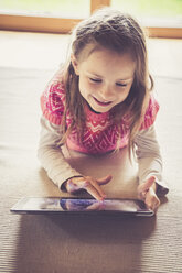 Portrait of little girl sitting on the floor using digital tablet - SARF000870