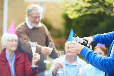 Älterer Mann gießt Champagner in ein Glas auf einer Geburtstags-Gartenparty - ZEF001030