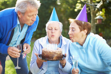 Senior woman blowing out candles on birthday cake - ZEF001036