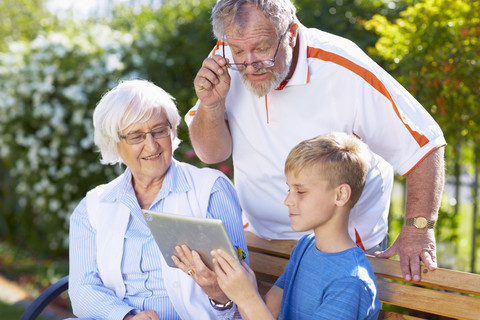 Enkel und Großeltern nutzen ein digitales Tablet im Park, lizenzfreies Stockfoto