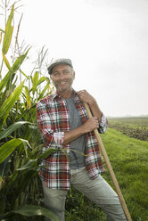 Porträt eines lächelnden Landwirts, der neben einem Maisfeld steht - UUF002020