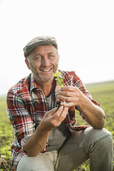 Porträt eines lächelnden Landwirts, der eine Pflanze auf einem Feld hält - UUF002022