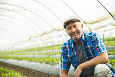 Portrait of smiling farmer crouching in a greenhouse - UUF002030