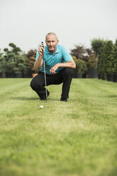 Golfspieler hockt auf dem Rasen und betrachtet den Golfball - UUF002037