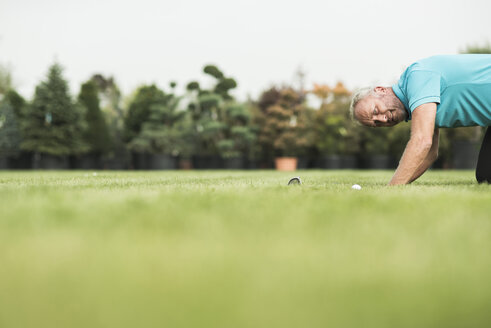 Golfspieler kniet auf dem Rasen und betrachtet den Golfball - UUF002040