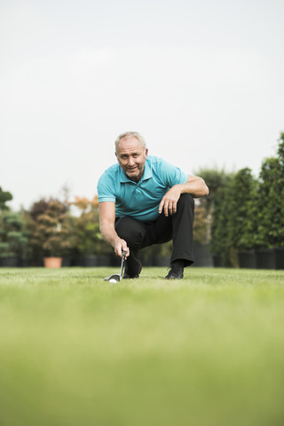 Golfspieler hockt auf dem Rasen und betrachtet den Golfball, lizenzfreies Stockfoto