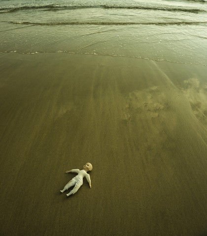 Puppe auf nassem Sandstrand am Wasser liegend, lizenzfreies Stockfoto