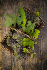 Weidenkorb mit Weintrauben und Weinblättern auf dunklem Holz - LVF001939