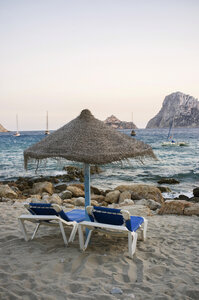 Spanien, Balearische Inseln, Ibiza, Cala Es Vedra, Sonnenliegen mit Sonnenschirm im Abendlicht - TKF000398
