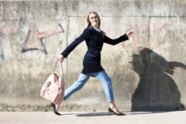 Junge Frau mit Samtblazer läuft vor einer Mauer - MAEF009192