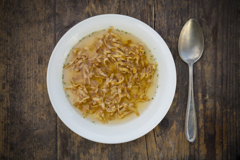 Schüssel mit schwäbischer Flädlesuppe und Löffel auf dunklem Holz, lizenzfreies Stockfoto