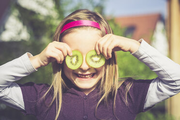 Laughing girl covering eyes with slices of kiwi - SARF000876