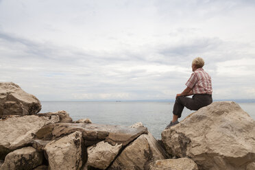 Slowenien, Piran, Frau sitzt auf Felsen am Ufer und schaut auf den Horizont - WIF001112