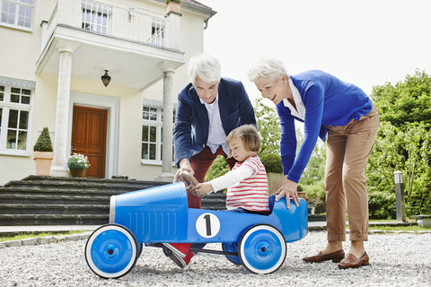 Deutschland, Hessen, Frankfurt, Älteres Ehepaar mit Enkelin sitzend Tretauto, lizenzfreies Stockfoto