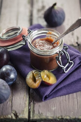 Opened preserving jar of plum fig jam on cloth and wood - SBDF001301