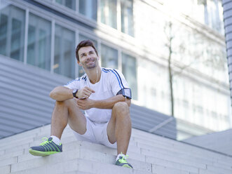 Smiling jogger with earphones sitting on stairs - MAD000069