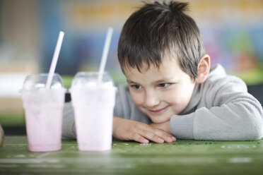 Lächelnder Junge mit Blick auf leere Milchshakebecher in einem Café - ZEF001254