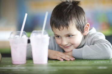 Smiling boy looking at empty milkshakecups in coffee shop - ZEF001254