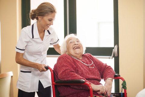 Krankenschwester kümmert sich um ältere Frau im Rollstuhl, lizenzfreies Stockfoto