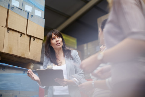 Woman with clipboard in warehouse talking to women stock photo