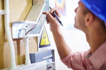 Electrician looking at wire at distribution board - ZEF001868