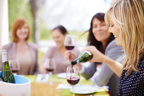Frau gießt ein Glas Rotwein mit Freunden im Hintergrund ein - ZEF001773