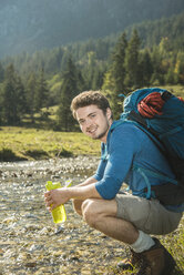 Österreich, Tirol, Tannheimer Tal, Porträt eines lächelnden jungen Wanderers mit Wasserflasche und Rucksack - UUF002101