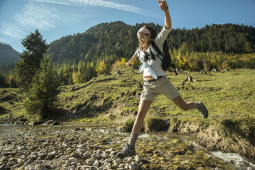 Austria, Tyrol, Tannheimer Tal, young female hiker crossing water - UUF002126