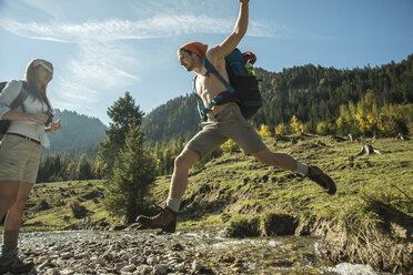 Österreich, Tirol, Tannheimer Tal, zwei junge Wanderer beim Überqueren von Wasser - UUF002127