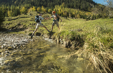 Österreich, Tirol, Tannheimer Tal, zwei junge Wanderer beim Überqueren von Wasser - UUF002129