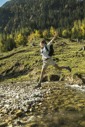 Österreich, Tirol, Tannheimer Tal, junge Wanderin beim Überqueren von Wasser - UUF002131