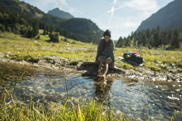 Austria, Tyrol, Tannheimer Tal, young female hiker relaxing at a brook - UUF002132