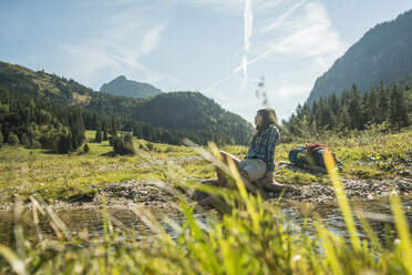 Austria, Tyrol, Tannheimer Tal, young female hiker relaxing at a brook - UUF002133