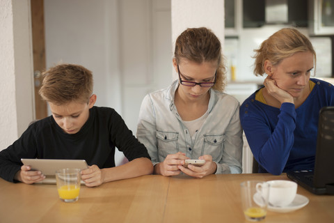 Mutter und ihre beiden Kinder entspannen sich zu Hause mit digitalem Tablet, Smartphone und Laptop, lizenzfreies Stockfoto