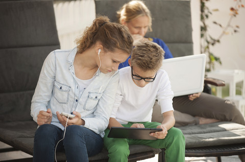 Mutter und ihre beiden Kinder entspannen sich mit Tablet, Smartphone und Laptop auf der Terrasse, lizenzfreies Stockfoto