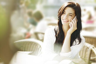 Smiling young woman telephoning with smartphone at a pavement cafe - GDF000470