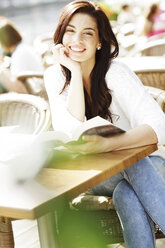 Glückliche junge Frau mit Buch in einem Straßencafé - GDF000472