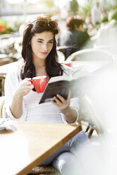 Lächelnde junge Frau liest ein Buch in einem Straßencafé - GDF000475